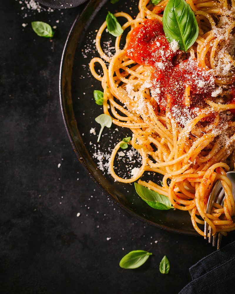 Tasty appetizing classic italian spaghetti pasta with tomato sauce, cheese parmesan and basil on plate on dark table. View from above, top view