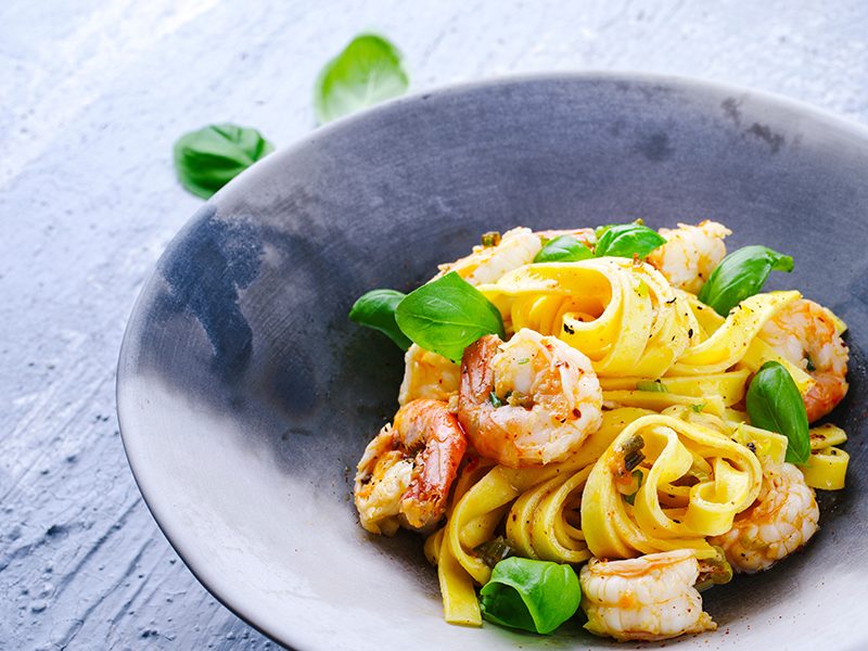 Traditionelle italienische Tagliatelle ai gamberoni Nudeln mit R Traditional Italian tagliatelle ai gamberoni pasta with king prawns and herbs served as close-up on a design plate with copy space